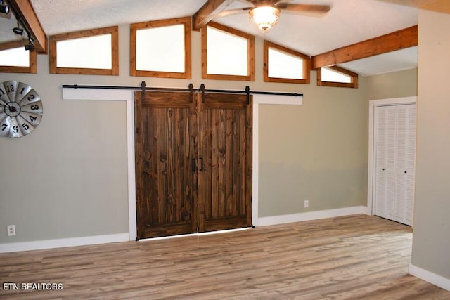 interior space with vaulted ceiling with beams, light hardwood / wood-style flooring, and a barn door