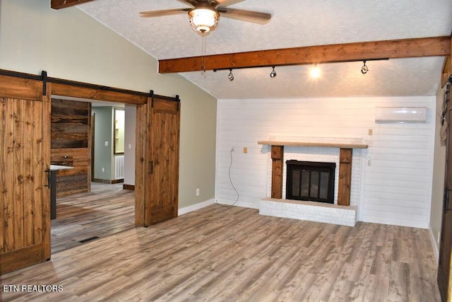 unfurnished living room with hardwood / wood-style flooring, a barn door, vaulted ceiling with beams, and a textured ceiling