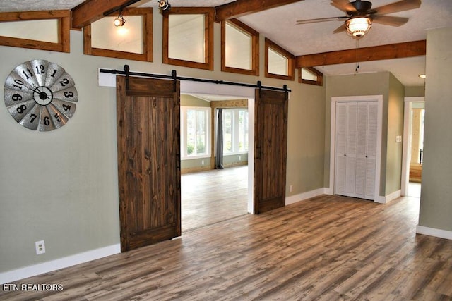 unfurnished room featuring ceiling fan, a barn door, hardwood / wood-style floors, and vaulted ceiling with beams