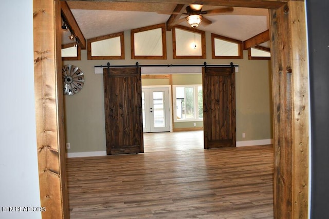 empty room with wood-type flooring, a barn door, and ceiling fan