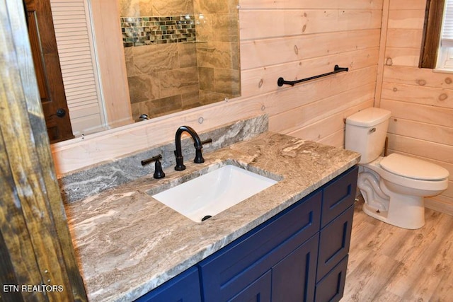 bathroom featuring hardwood / wood-style flooring, vanity, toilet, and wood walls