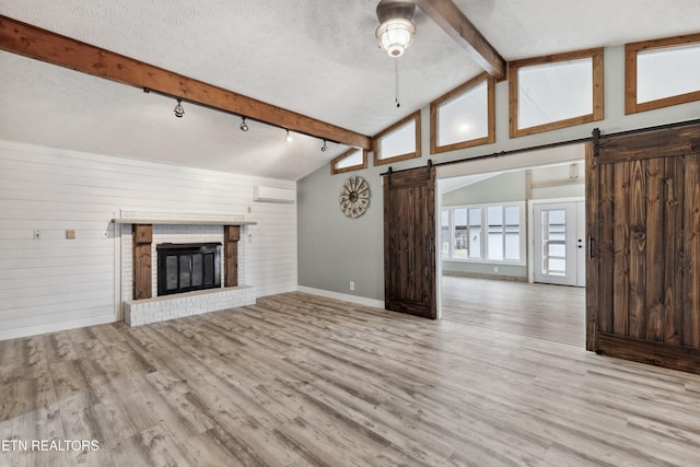 unfurnished living room featuring beam ceiling, light hardwood / wood-style flooring, an AC wall unit, a textured ceiling, and a barn door