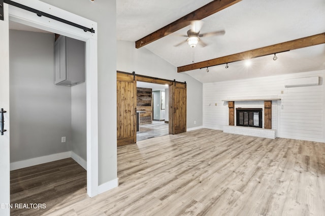 unfurnished living room with ceiling fan, light hardwood / wood-style floors, a fireplace, a barn door, and a wall unit AC