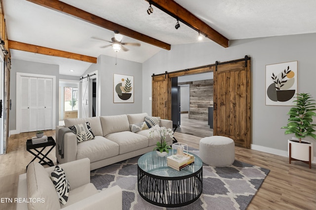 living room featuring a barn door, light hardwood / wood-style floors, vaulted ceiling with beams, ceiling fan, and a textured ceiling