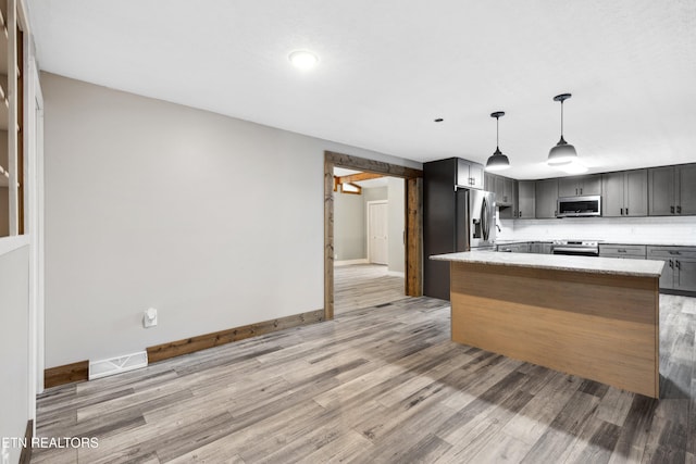 kitchen with appliances with stainless steel finishes, backsplash, light stone counters, pendant lighting, and light hardwood / wood-style floors