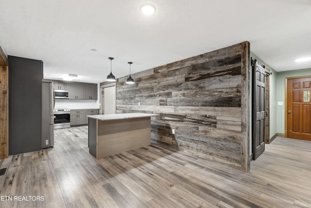 kitchen with gray cabinetry, light hardwood / wood-style flooring, a barn door, wood walls, and appliances with stainless steel finishes