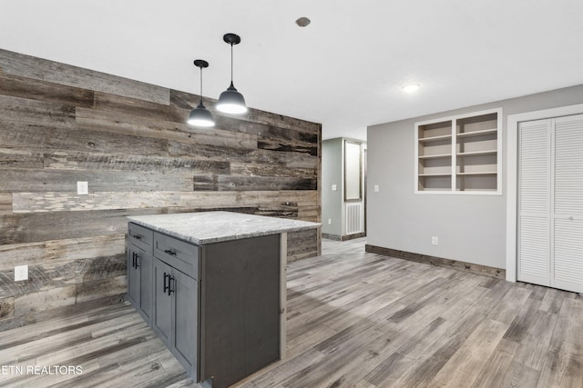 kitchen featuring light stone counters, pendant lighting, a kitchen island, wood walls, and gray cabinets