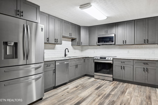 kitchen featuring appliances with stainless steel finishes, light wood-type flooring, light stone counters, gray cabinets, and sink