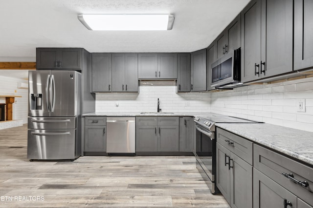 kitchen featuring appliances with stainless steel finishes, gray cabinetry, light wood-type flooring, light stone countertops, and sink