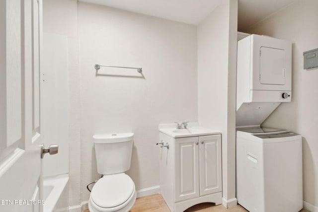 bathroom with stacked washer / dryer, toilet, hardwood / wood-style floors, and vanity