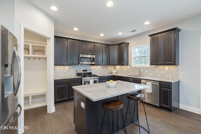 kitchen with sink, stainless steel appliances, light stone counters, a kitchen island, and dark hardwood / wood-style flooring