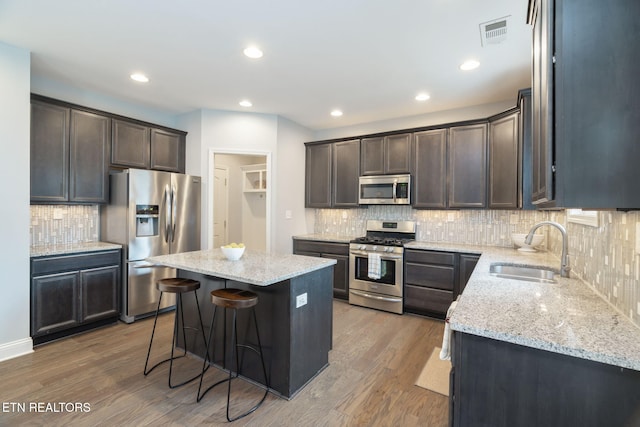 kitchen featuring sink, appliances with stainless steel finishes, light stone counters, wood-type flooring, and a kitchen island