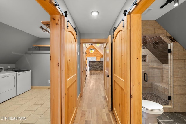 interior space featuring toilet, separate washer and dryer, vaulted ceiling, a shower with door, and hardwood / wood-style floors