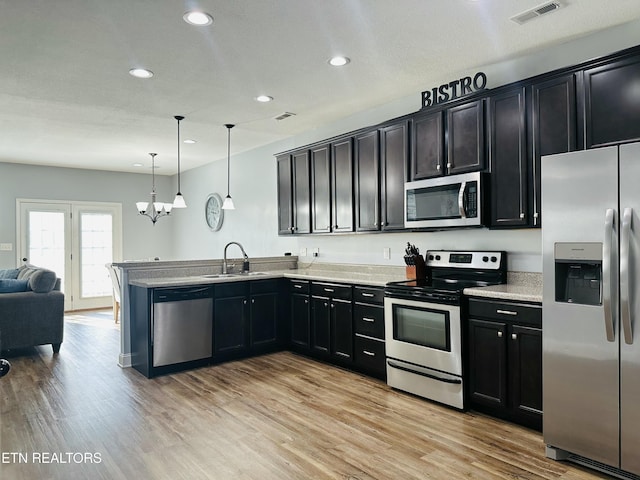 kitchen with stainless steel appliances, a peninsula, open floor plan, hanging light fixtures, and light wood finished floors