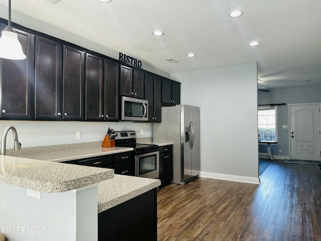 kitchen with a peninsula, dark wood-type flooring, stainless steel appliances, light countertops, and decorative light fixtures