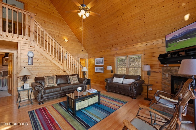 living room with high vaulted ceiling, a fireplace, light hardwood / wood-style floors, and wood walls