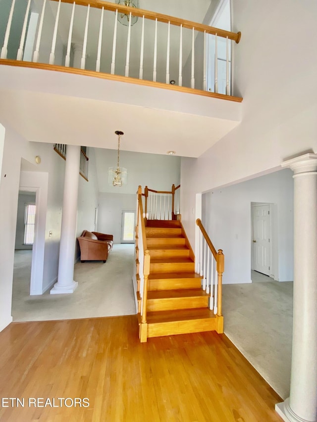 stairway with a towering ceiling, carpet flooring, and decorative columns