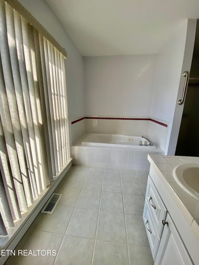 bathroom featuring tile patterned flooring, tiled tub, and vanity