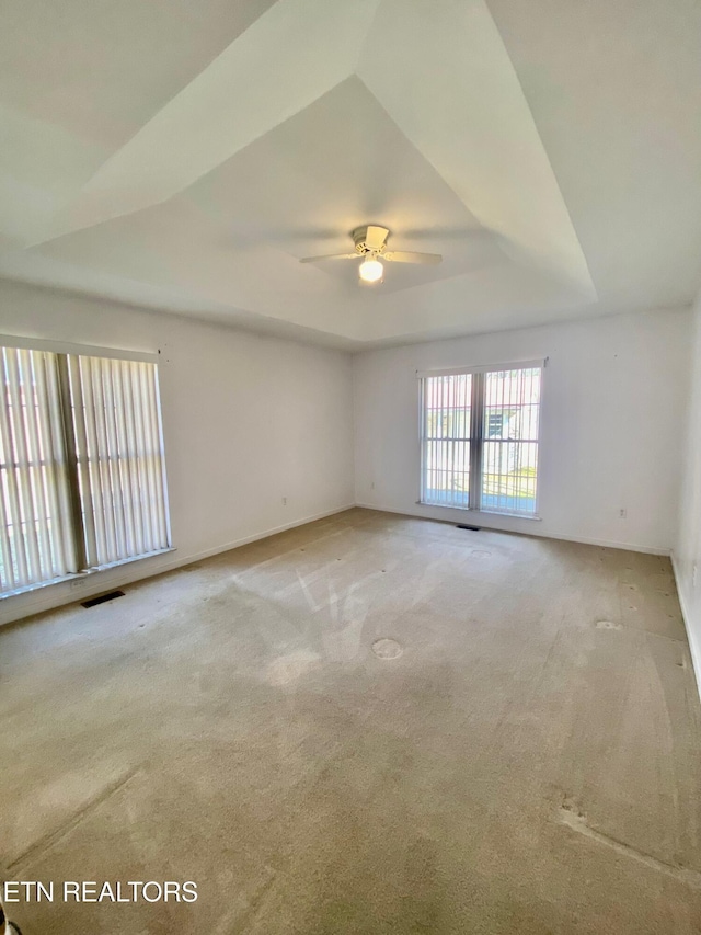 empty room with light colored carpet, ceiling fan, and a tray ceiling