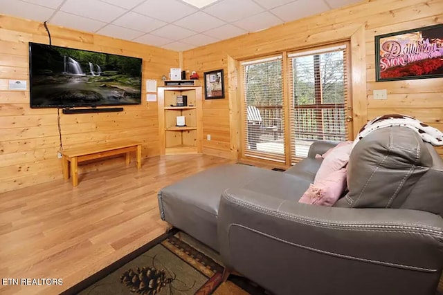 living room featuring wood-type flooring, a paneled ceiling, and wood walls