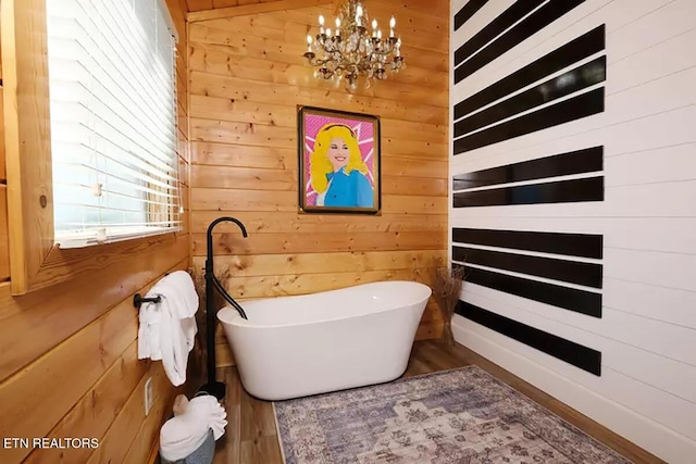 bathroom featuring a notable chandelier, wooden walls, hardwood / wood-style floors, and a tub