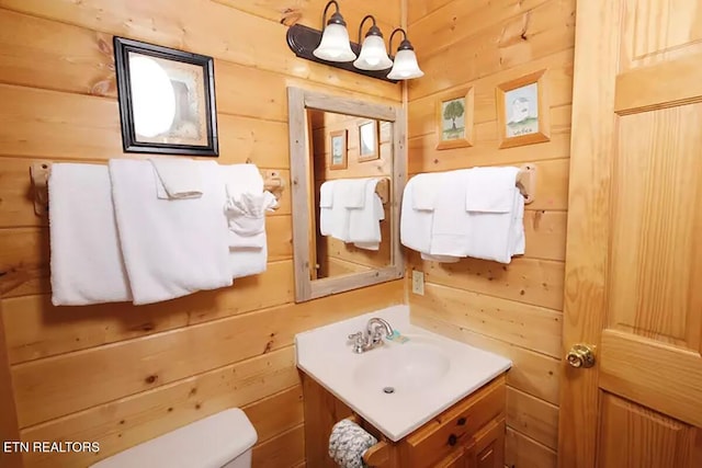 bathroom with toilet, vanity, and wooden walls