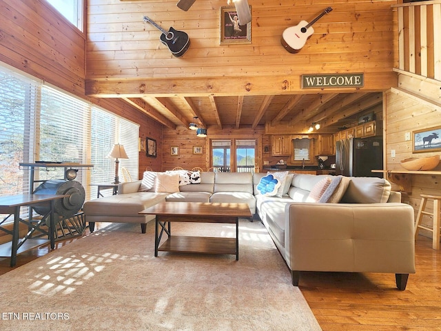 living room with beamed ceiling, a towering ceiling, wooden walls, and light hardwood / wood-style floors