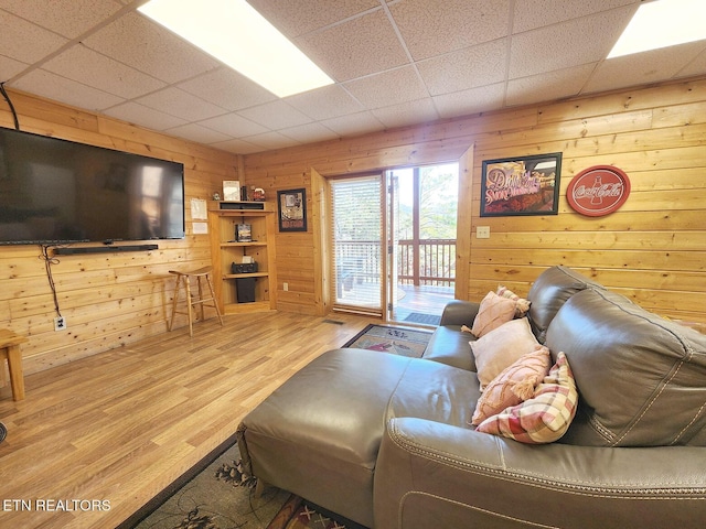 living room featuring a drop ceiling, wooden walls, and light wood-type flooring