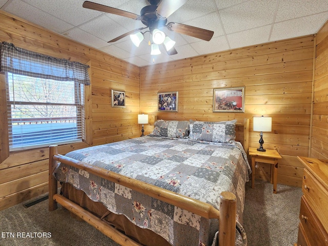 bedroom featuring ceiling fan, a paneled ceiling, carpet floors, and wood walls