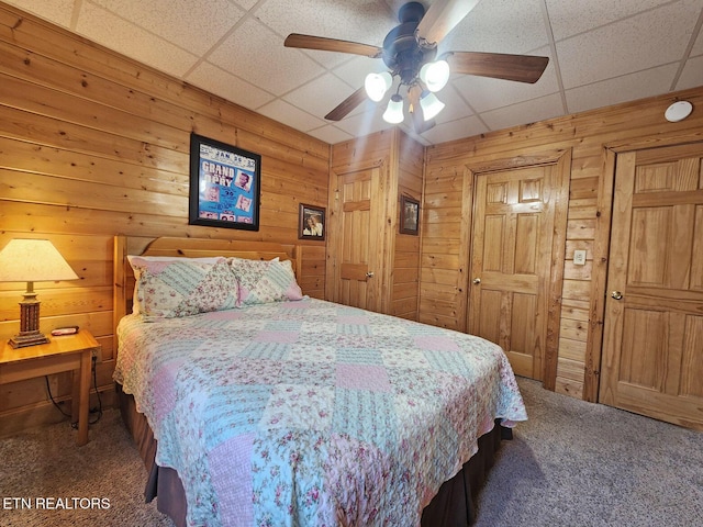 bedroom with ceiling fan, wooden walls, carpet floors, and a drop ceiling