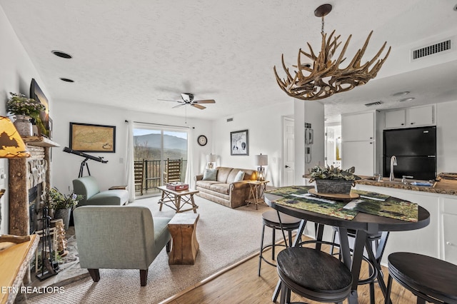 living room with ceiling fan, light hardwood / wood-style floors, sink, and a textured ceiling