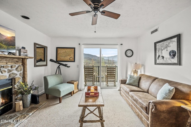 living room with a mountain view, a stone fireplace, a textured ceiling, and carpet