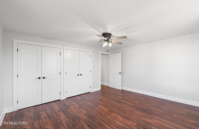 unfurnished bedroom featuring ceiling fan, dark hardwood / wood-style floors, a textured ceiling, and two closets