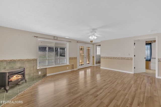 unfurnished living room with ceiling fan, light hardwood / wood-style floors, and a wood stove