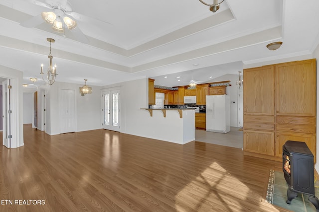 unfurnished living room featuring ceiling fan with notable chandelier, a wood stove, hardwood / wood-style flooring, ornamental molding, and a raised ceiling