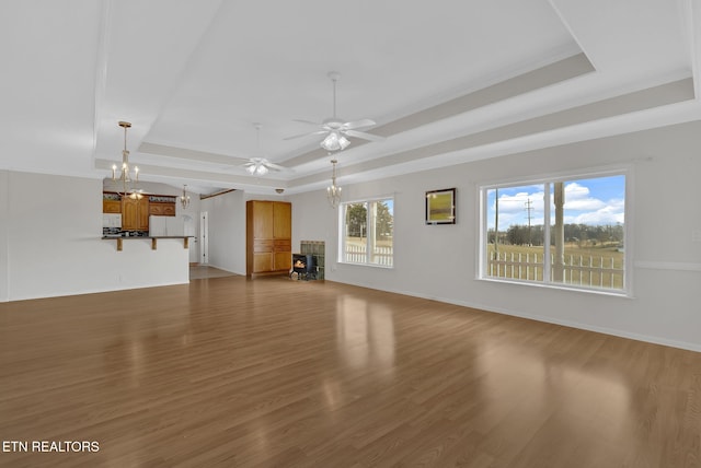 unfurnished living room featuring dark wood-type flooring, ceiling fan with notable chandelier, and a tray ceiling