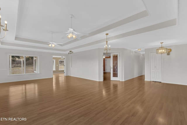 unfurnished living room with dark wood-type flooring, ornamental molding, a tray ceiling, and ceiling fan with notable chandelier