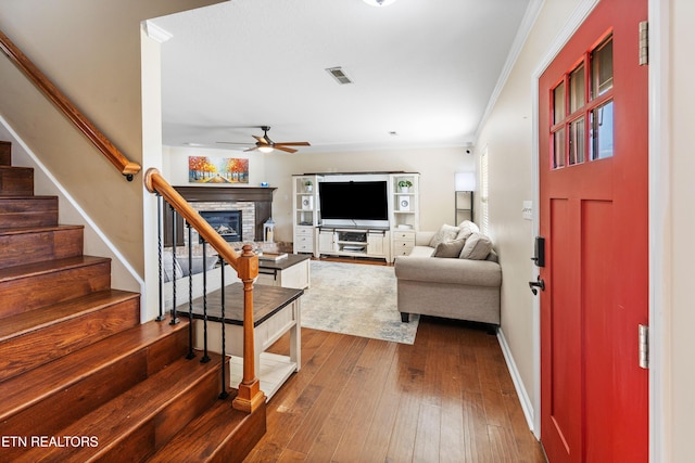 living room with dark wood-type flooring, a fireplace, crown molding, and ceiling fan