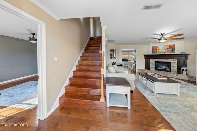 stairs with hardwood / wood-style flooring, ornamental molding, ceiling fan, and a fireplace