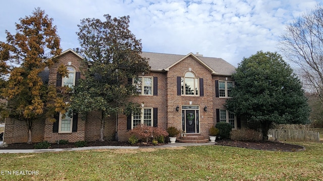 colonial-style house featuring brick siding, a front yard, and fence