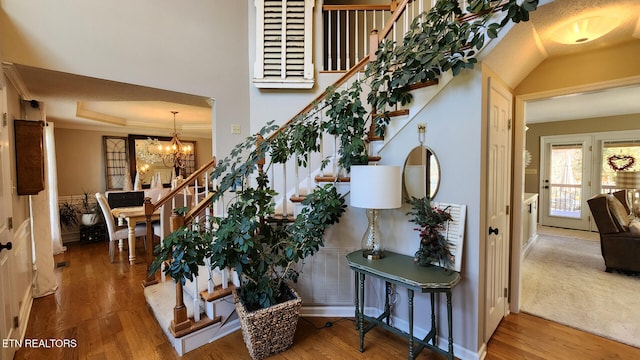 stairway featuring a tray ceiling, wood finished floors, crown molding, and an inviting chandelier