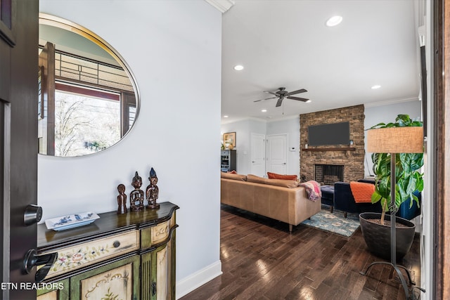 living room with dark hardwood / wood-style floors, ceiling fan, ornamental molding, and a stone fireplace