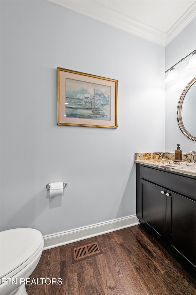 bathroom with wood-type flooring, ornamental molding, vanity, and toilet