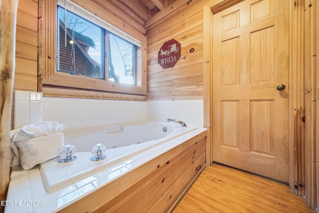 bathroom featuring hardwood / wood-style flooring, wooden walls, and a bathtub