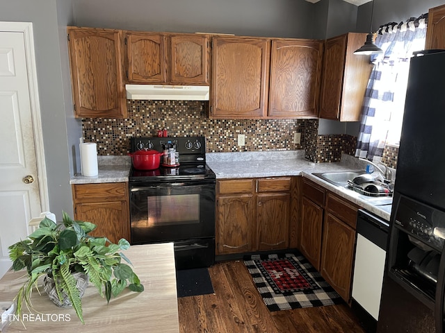 kitchen with sink, dark wood-type flooring, hanging light fixtures, backsplash, and black appliances