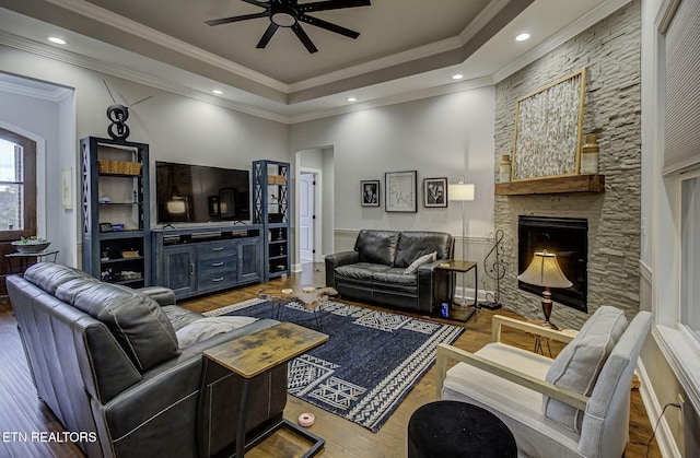 living room featuring hardwood / wood-style flooring, crown molding, a raised ceiling, and a fireplace