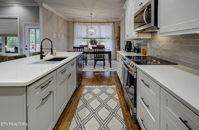 kitchen featuring appliances with stainless steel finishes, decorative light fixtures, sink, ornamental molding, and a kitchen island with sink