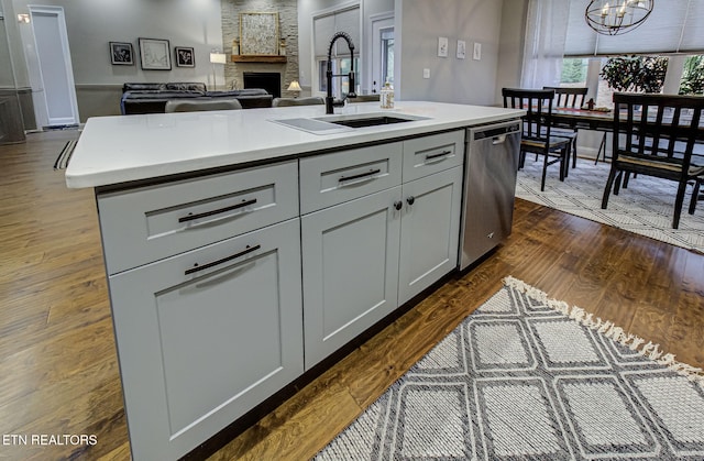 kitchen with sink, a center island with sink, stainless steel dishwasher, dark hardwood / wood-style floors, and gray cabinets