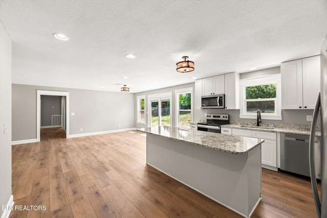 kitchen with sink, a center island, stainless steel appliances, light stone countertops, and white cabinets