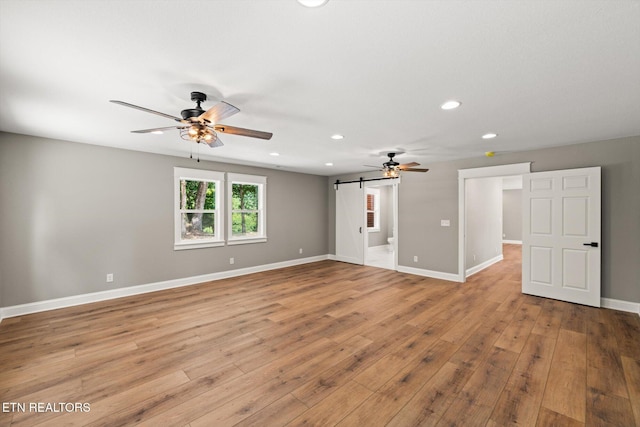 unfurnished room with ceiling fan, a barn door, and light hardwood / wood-style floors